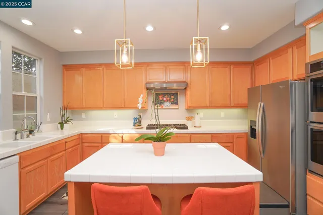 a kitchen with stainless steel appliances granite countertop a sink a stove a refrigerator cabinets and chairs