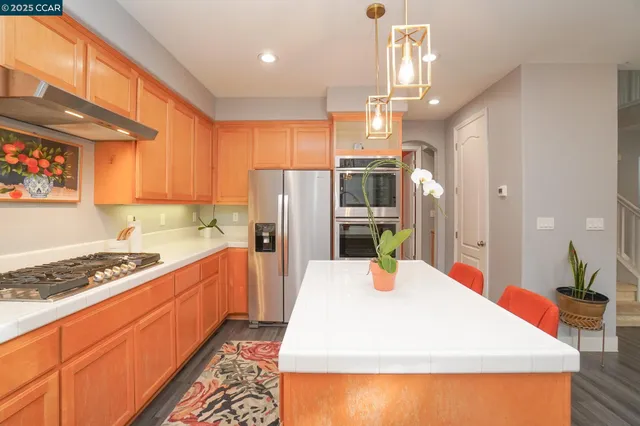 a kitchen with stainless steel appliances kitchen island granite countertop a refrigerator a stove top oven a sink dishwasher and dining table