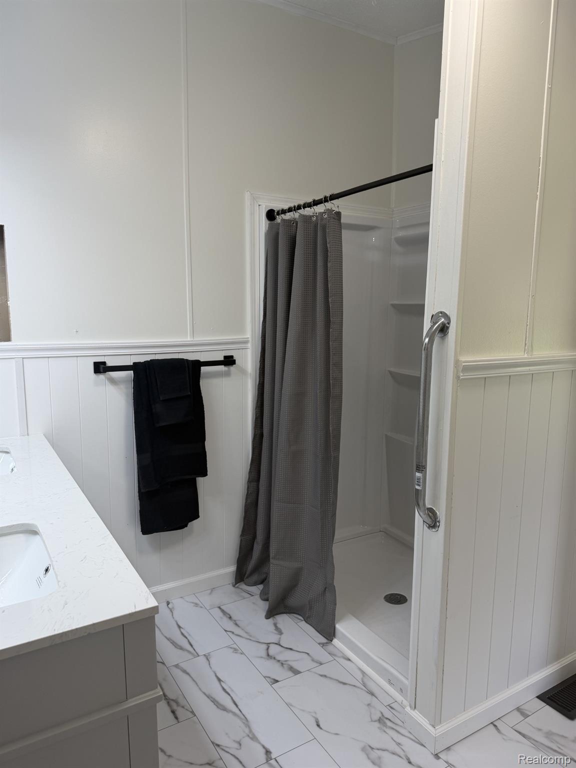 3586 Columbiaville Road Columbiaville, MI 48421 - Photo 8 of 10 Bathroom featuring a white shower stall with an integrated grab bar, white wainscoting, and large format marble-look tile flooring