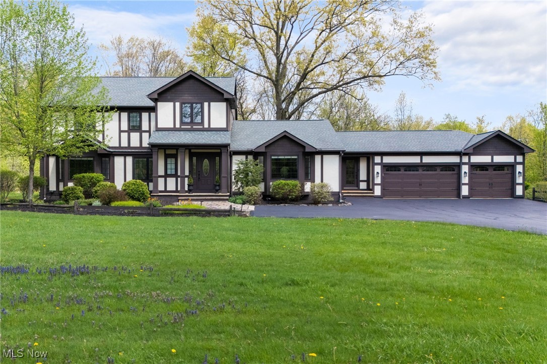 View of front of property featuring an attached garage, a shingled roof, asphalt driveway, and a front lawn