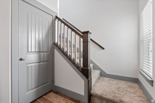 7822 North Copperbend Road Eagle Mountain, UT 84005 - Photo 7 of 46 Carpeted staircase with wood newel post and handrail, featuring a paneled interior door, wood-finish flooring, and window blinds