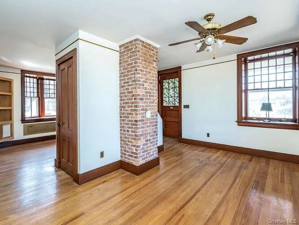 an empty room with wooden floor chandelier fan and windows