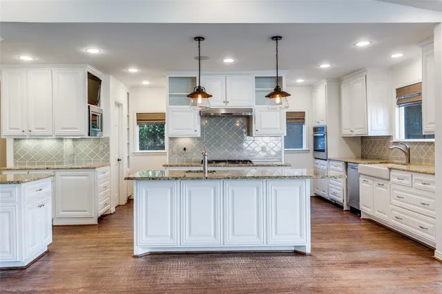a kitchen with kitchen island granite countertop a stove a sink and white cabinets with wooden floor