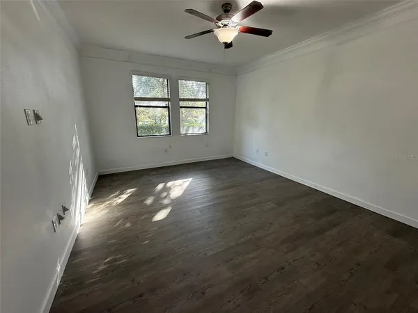 an empty room with wooden floor chandelier fan and windows