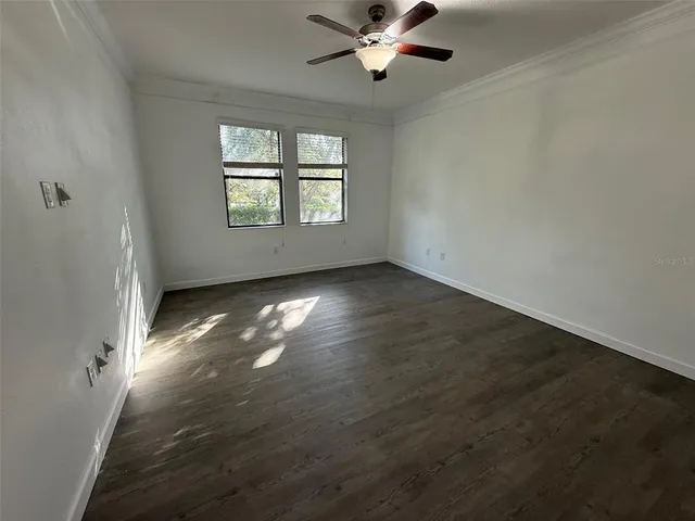 an empty room with wooden floor chandelier fan and windows