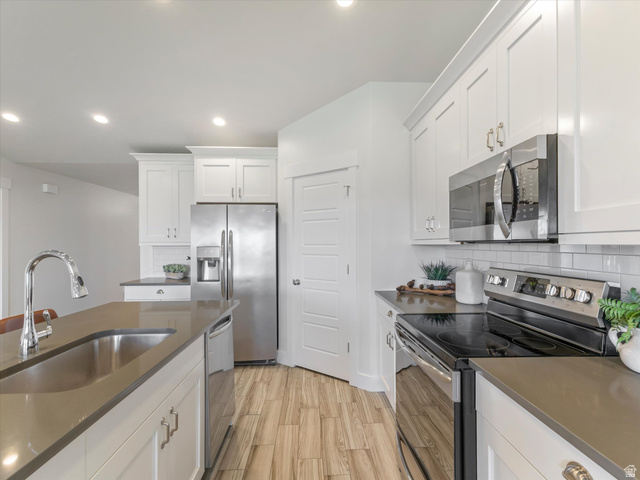 1278 South Grace Way Layton, UT 84041 - Photo 3 of 23 Modern kitchen featuring a large island with an undermount sink, stainless steel appliances, white shaker cabinetry, light-colored countertops, and wood-finish flooring