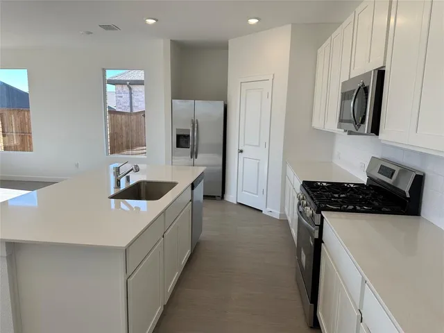 a kitchen with stainless steel appliances a refrigerator a stove top oven a sink and white cabinets