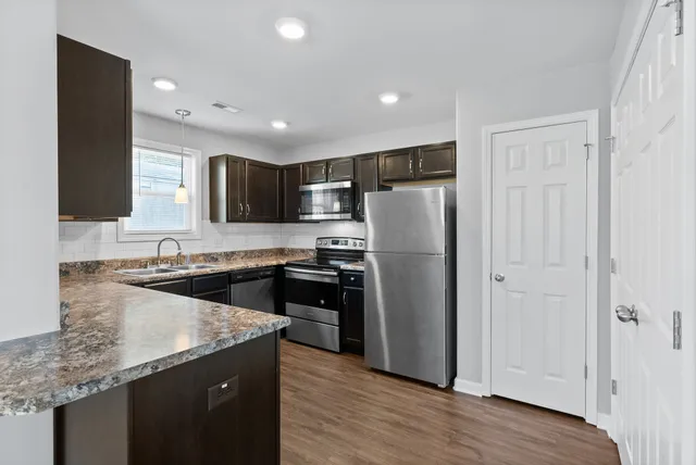 a kitchen with granite countertop stainless steel appliances a refrigerator a sink and wooden cabinets