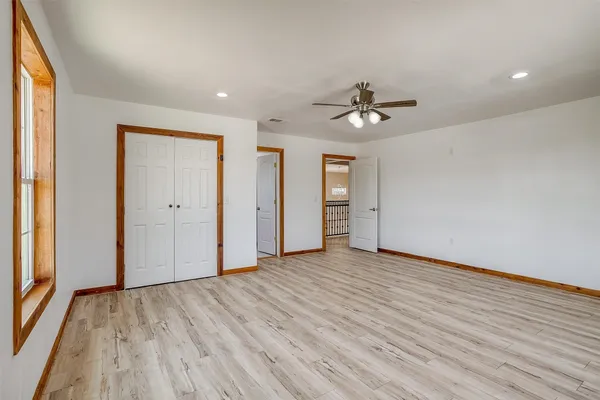 an empty room with wooden floor ceiling fan and windows