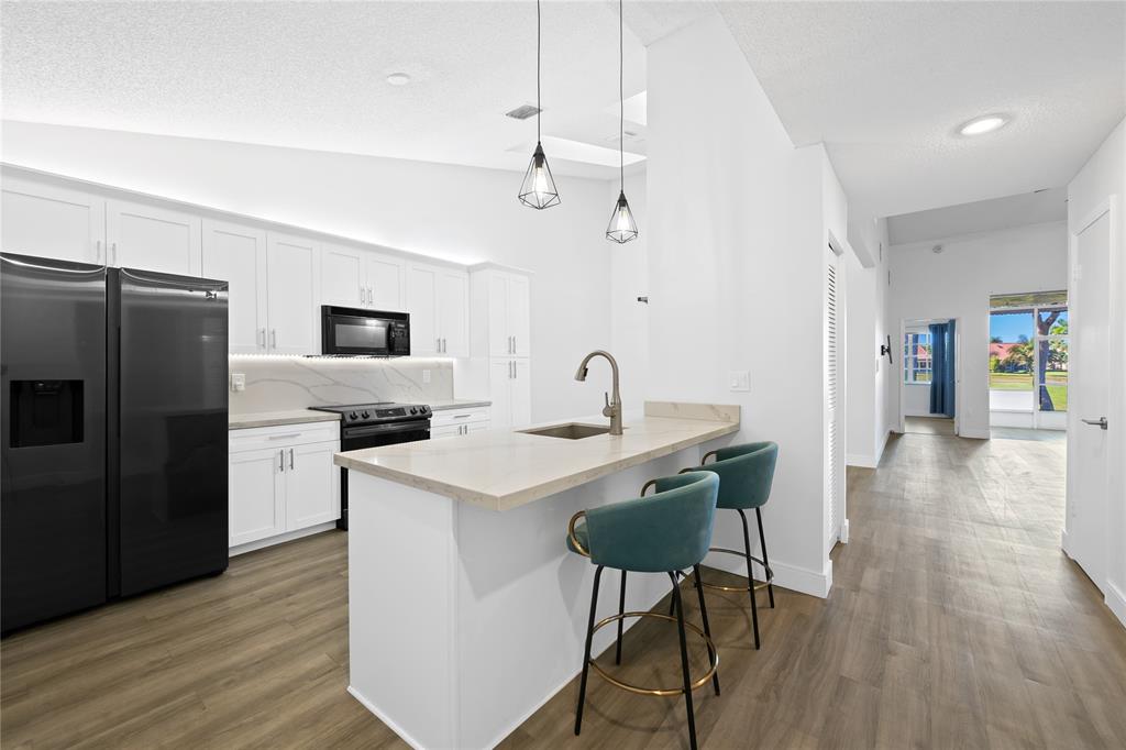 8245 Northwest 70th Street Tamarac, FL 33321 - Photo 3 of 29 a kitchen with a sink a refrigerator a stove and white cabinets with wooden floor