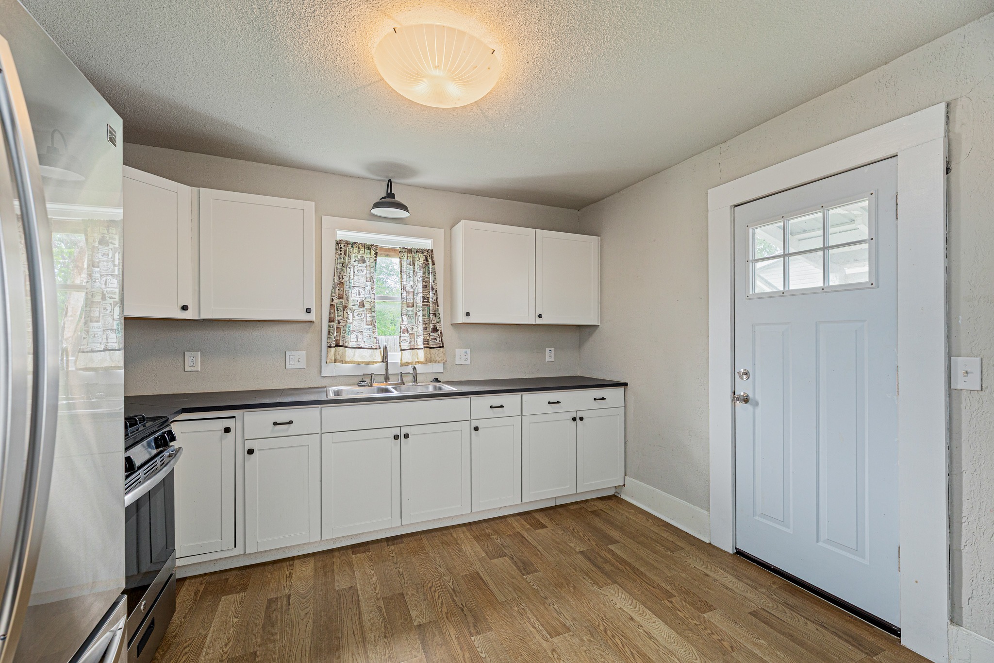 322 Blanco Avenue Luling, TX 78648 - Photo 7 of 20 A compact kitchen with sleek white cabinetry, dark counters, and light wood flooring.