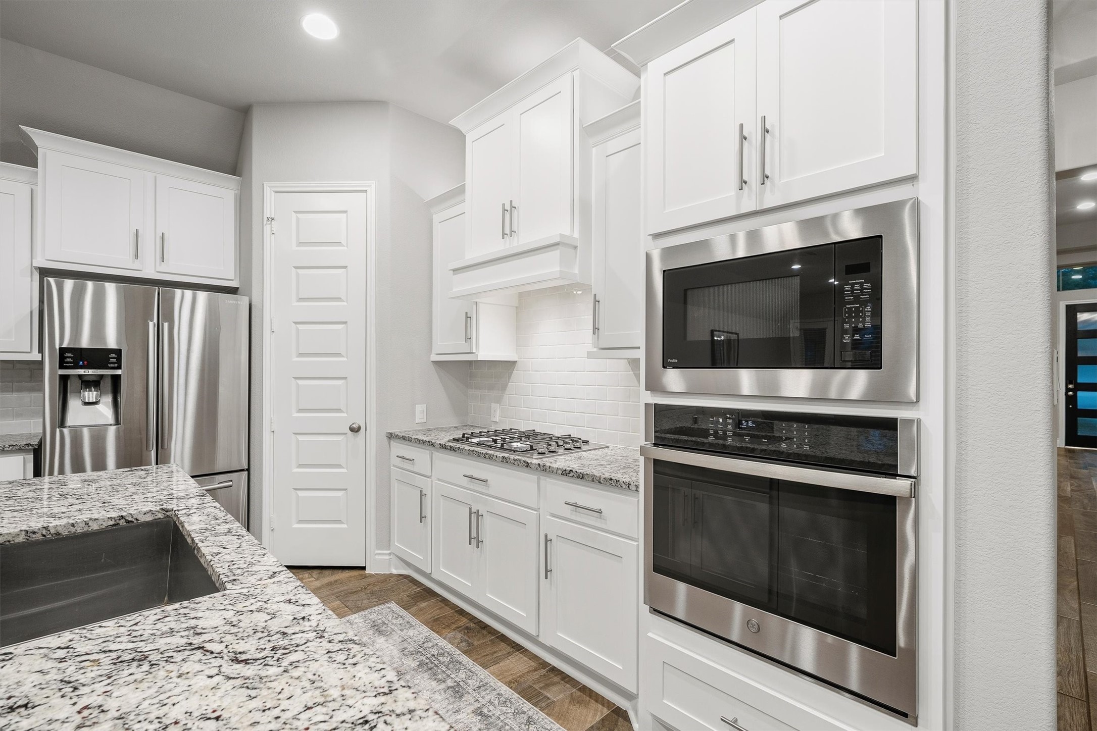 29118 Lantana Ridge Court Fulshear, TX 77441 - Photo 6 of 29 Another view of this gorgeous kitchen highlights the built-in stainless steel appliances, sleek modern white backsplash, and a stylish hooded vent, showcasing the kitchen’s contemporary design and high-end finishes.