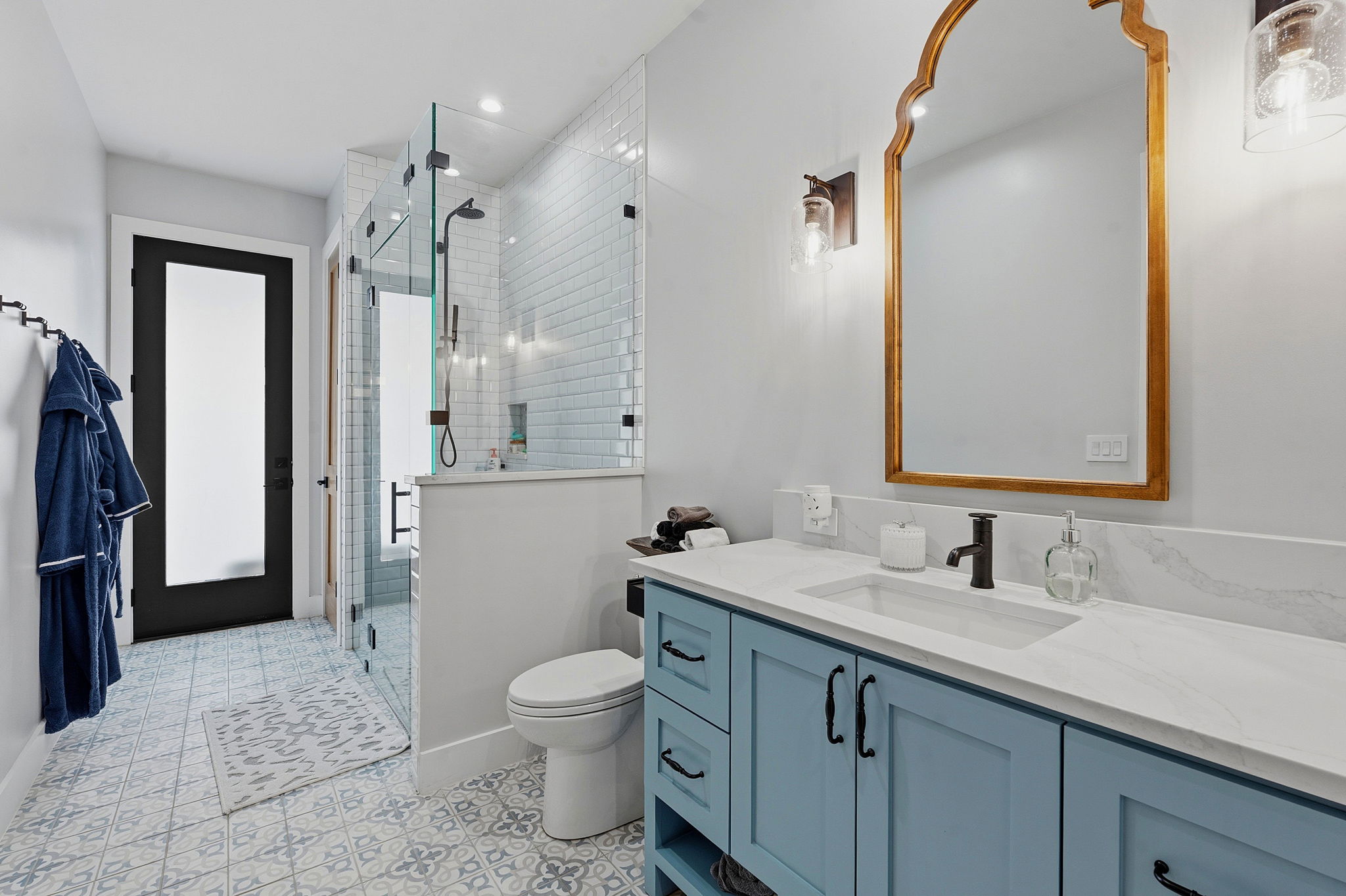 194 Placid Way Spring Branch, TX 78070 - Photo 25 of 37 Spacious bathroom featuring a glass-enclosed shower with subway tile, a light blue vanity with a quartz countertop, a decorative gold-framed mirror, and patterned floor tiling