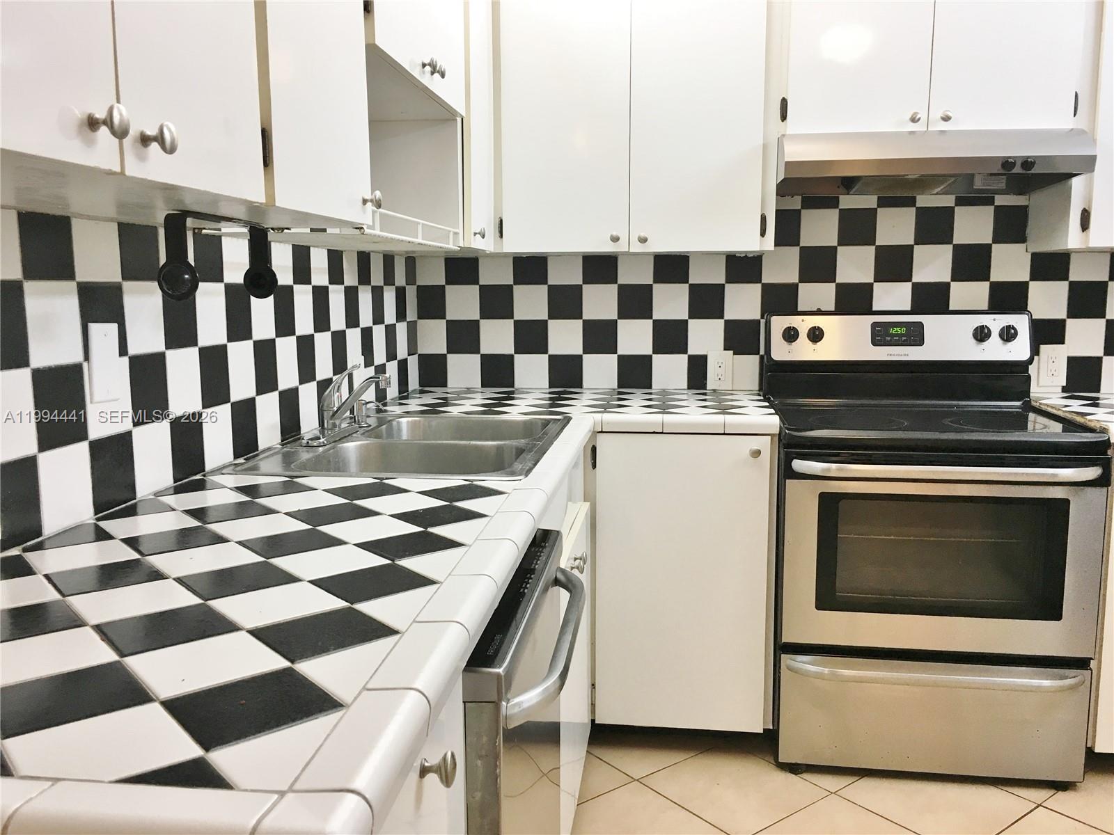 5831 Southwest 62nd Street, Unit WEST Miami, FL 33143 - Photo 5 of 16 a kitchen with a checkered floor and white cabinets