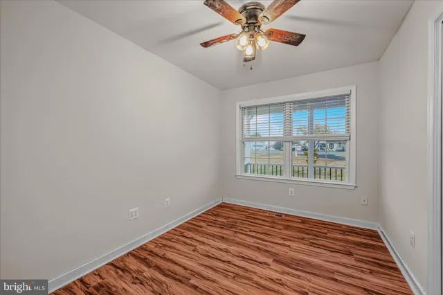 an empty room with wooden floor chandelier fan and windows