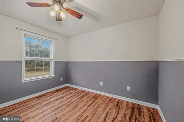an empty room with wooden floor chandelier fan and windows