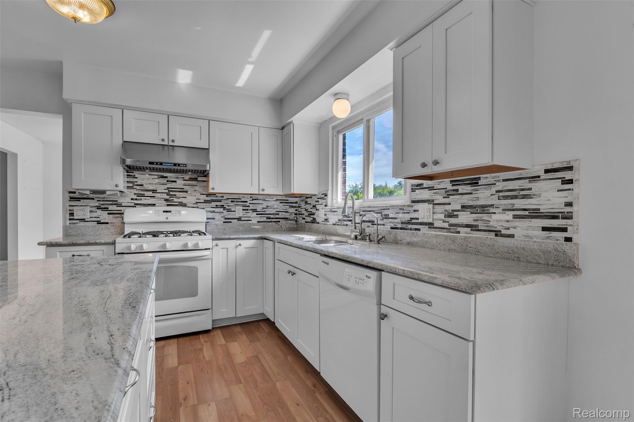 7000 Woonsocket Street Canton, MI 48187 - Photo 20 of 65 Contemporary kitchen featuring white cabinetry, light-toned countertops, a mosaic tile backsplash, wood-finish flooring, and a stainless steel range hood