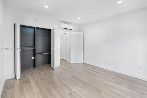 a view of an empty room with wooden floor and a kitchen