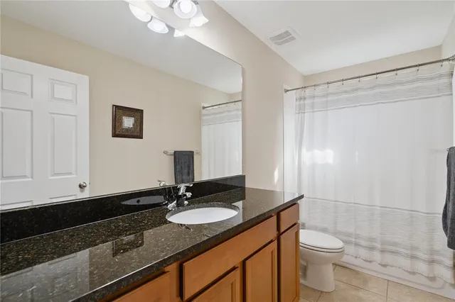 a bathroom with a granite countertop sink a toilet a mirror and shower