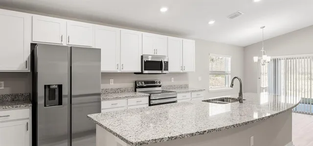 a kitchen with granite countertop a refrigerator a sink a stove a counter space and cabinets