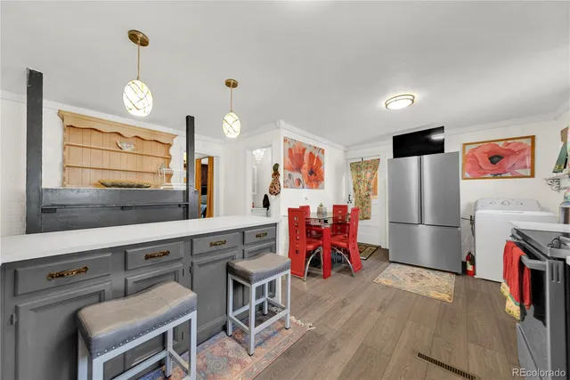 a kitchen with granite countertop a refrigerator a stove a sink a dining table and chairs with wooden floor