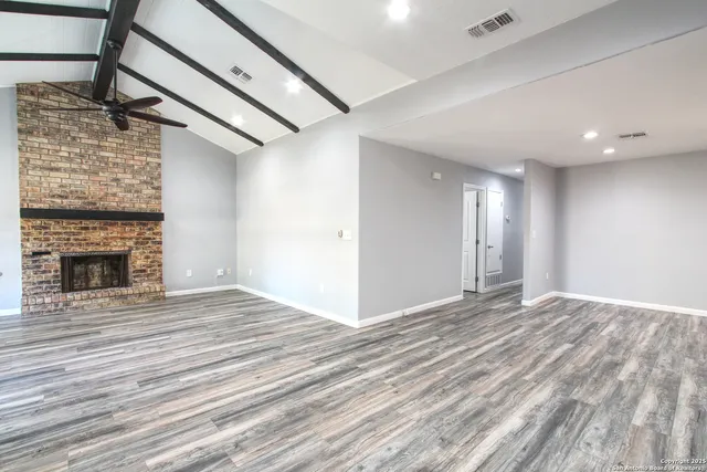 a view of an empty room with wooden floor fireplace and a window