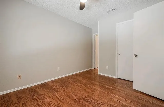 a view of an empty room with window and hardwood floor