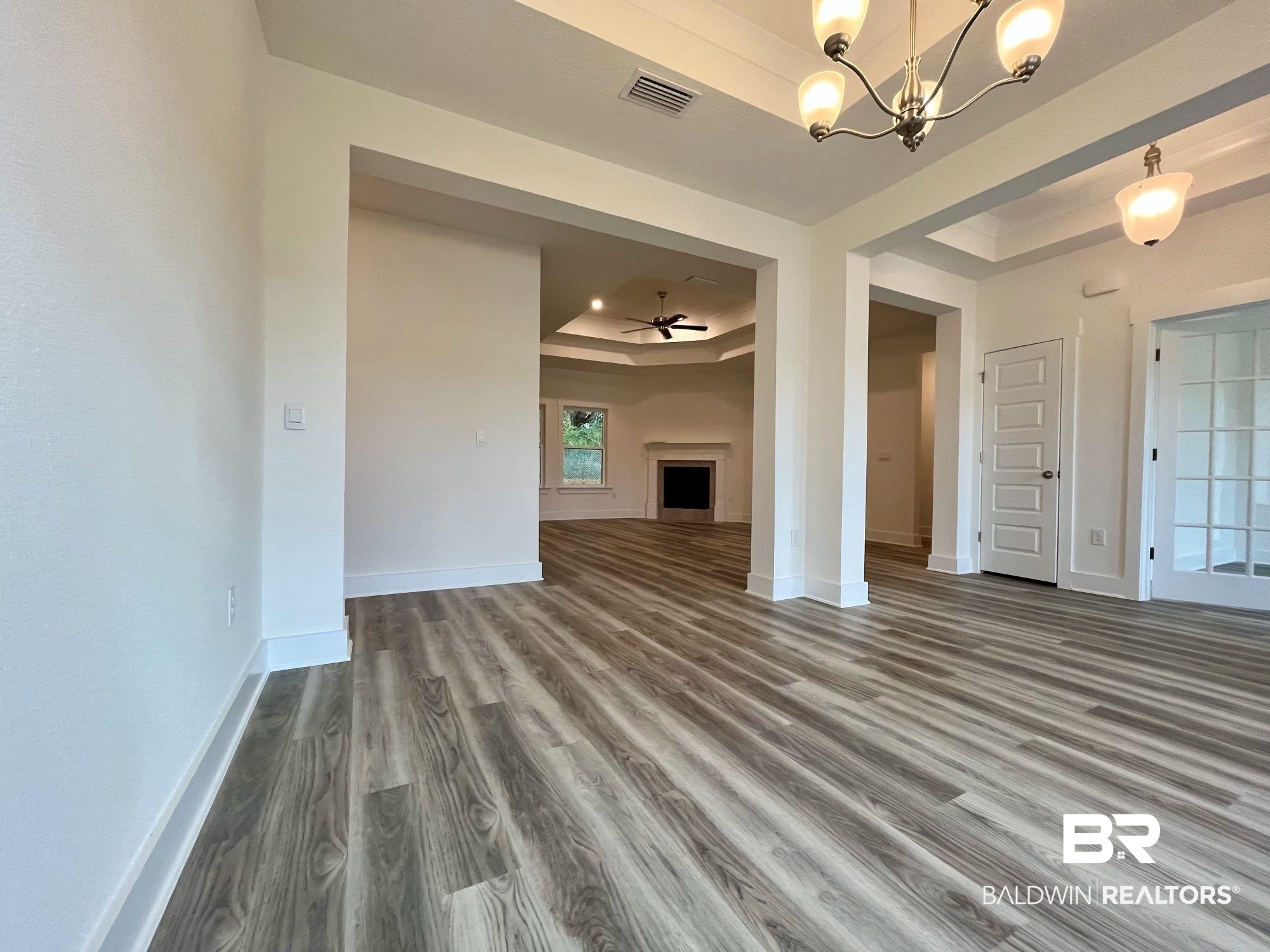 334 Barndling Street Fairhope, AL 36532 - Photo 9 of 34 Unfurnished living room with hardwood / wood-style floors, ceiling fan with notable chandelier, and a raised ceiling