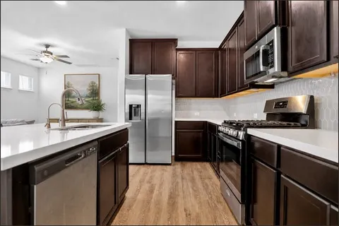 a kitchen with stainless steel appliances a sink dishwasher a refrigerator a stove top oven a sink and dishwasher with wooden floor