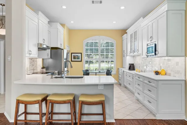 a large white kitchen with granite countertop a stove a sink a window and white cabinets