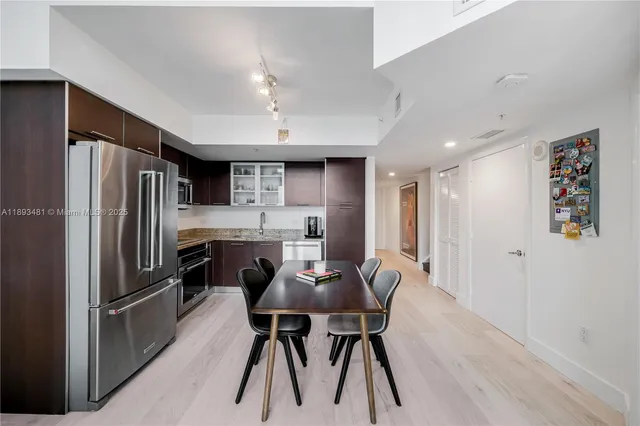 a kitchen with stainless steel appliances a refrigerator a stove a dining table and chairs with wooden floor