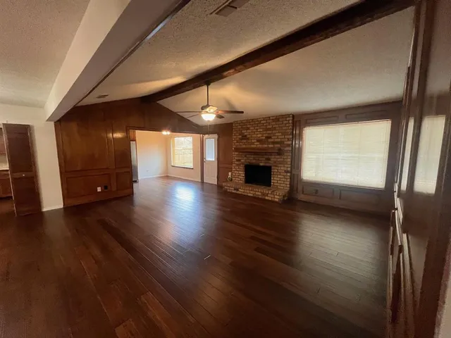 a view of an empty room and a kitchen with wooden floor and a window