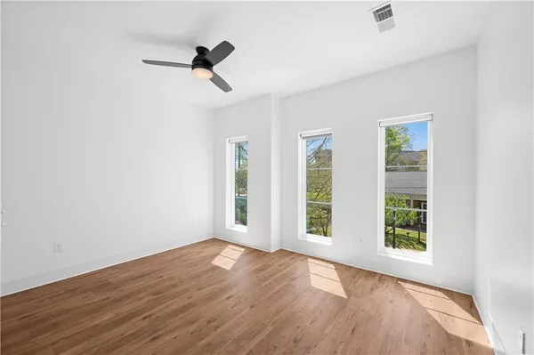an empty room with wooden floor fan and windows