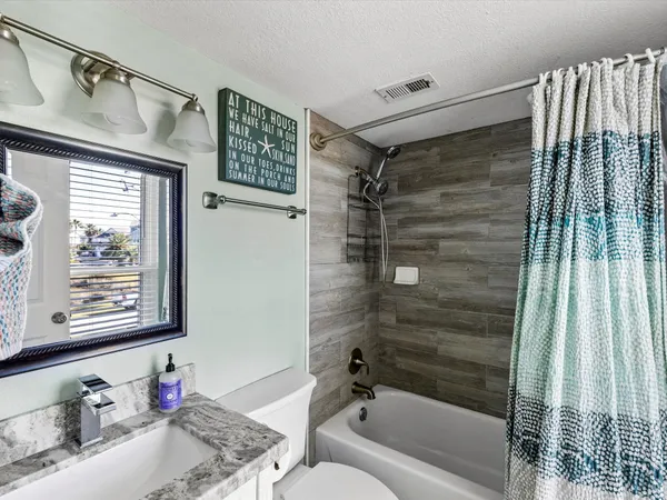 a bathroom with a granite countertop bathtub shower sink vanity and toilet