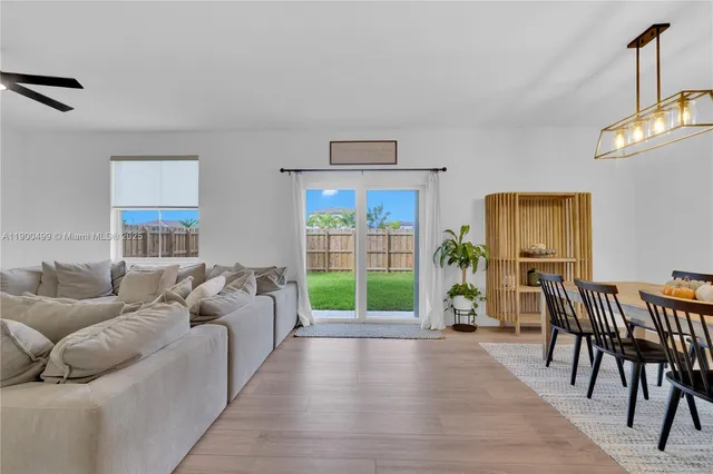 a living room with furniture two large windows and a dining table
