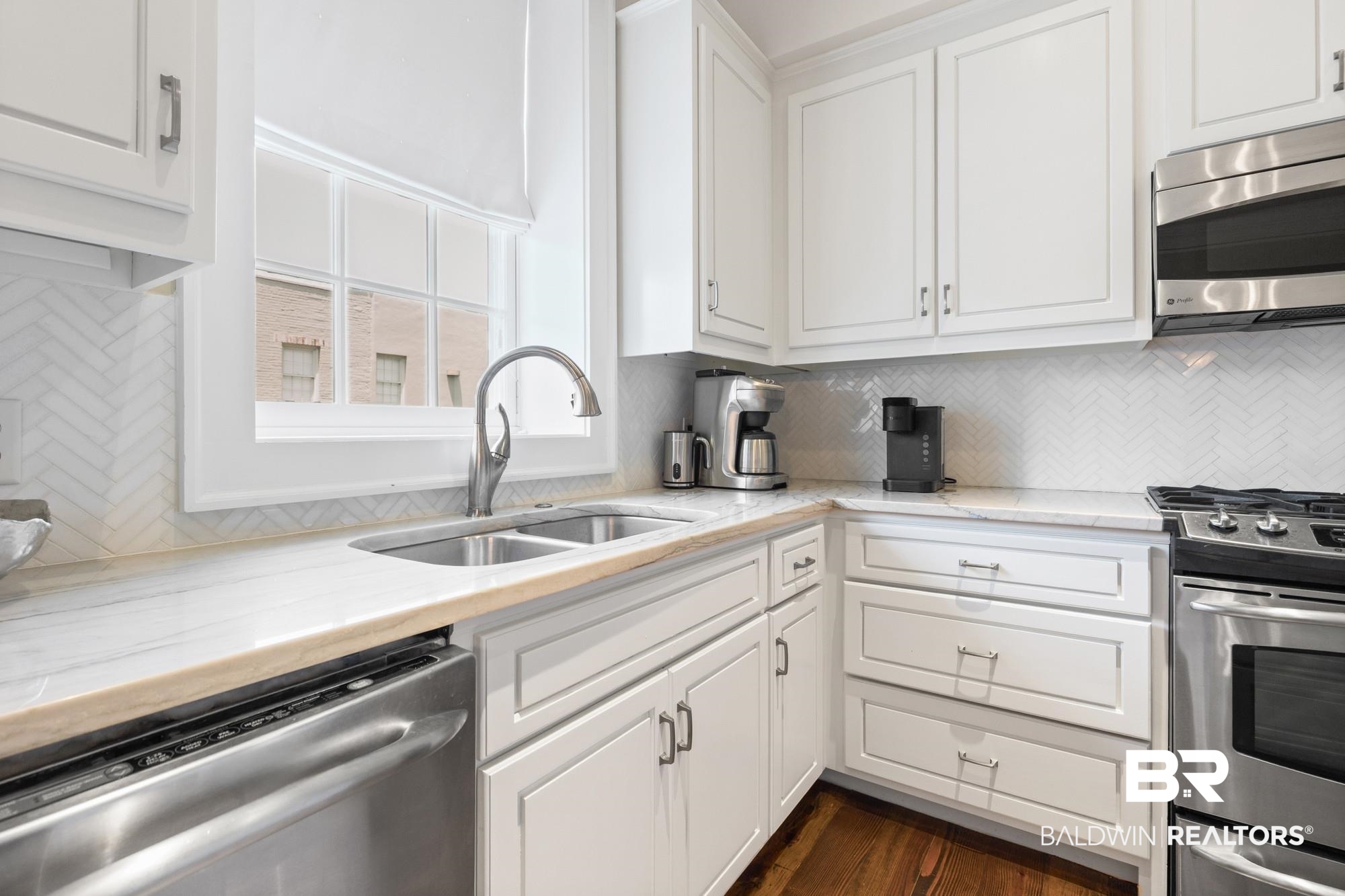 701 Dauphin Street, Unit A Mobile, AL 36602 - Photo 16 of 31 Bright kitchen featuring white shaker-style cabinetry, a double basin stainless steel sink, white stone countertops, and a white herringbone tile backsplash