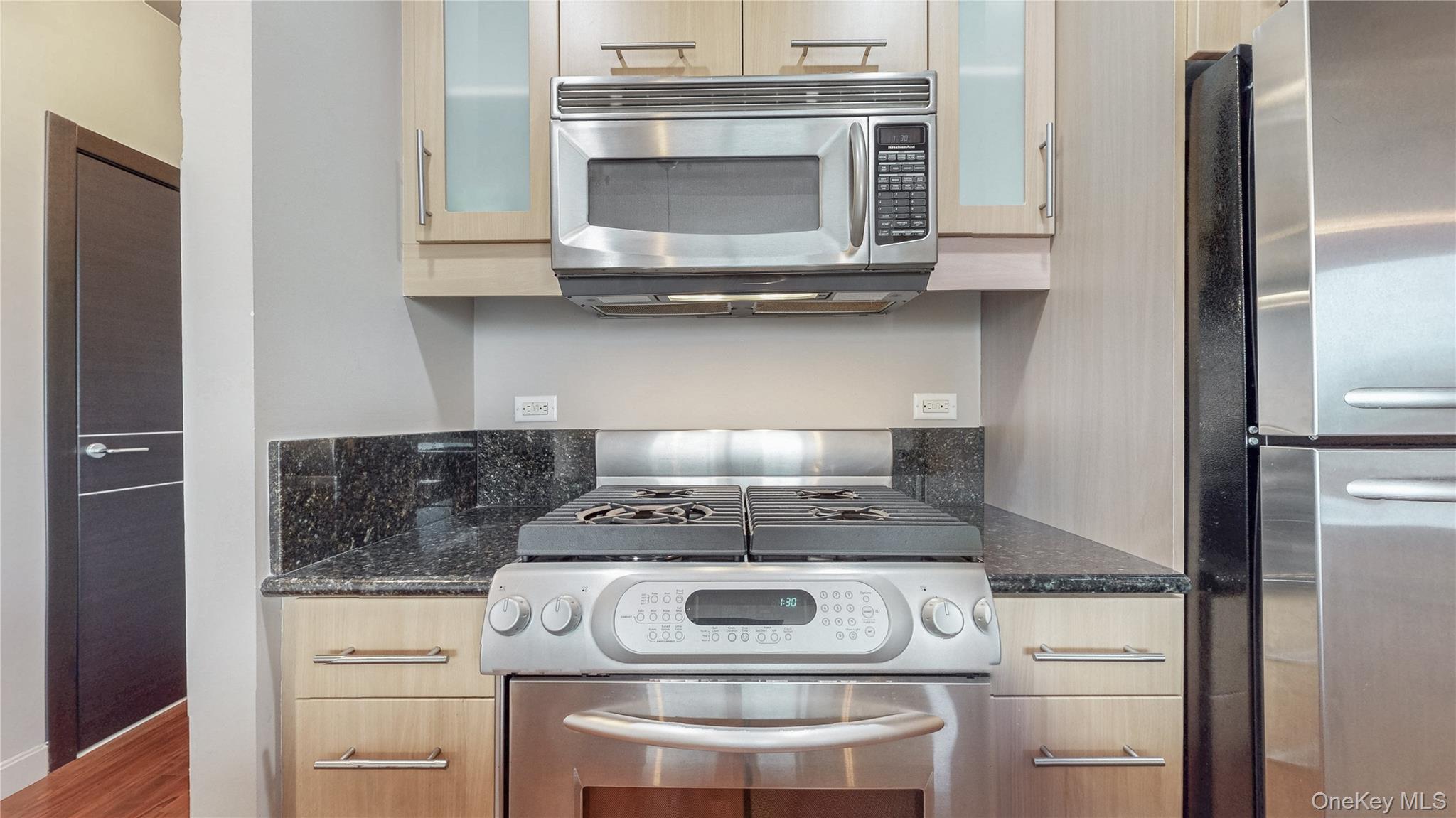 10724 71st Road, Unit 7E Queens, NY 11375 - Photo 5 of 21 Kitchen with stainless steel appliances, glass insert cabinets, dark stone counters, and wood finished floors