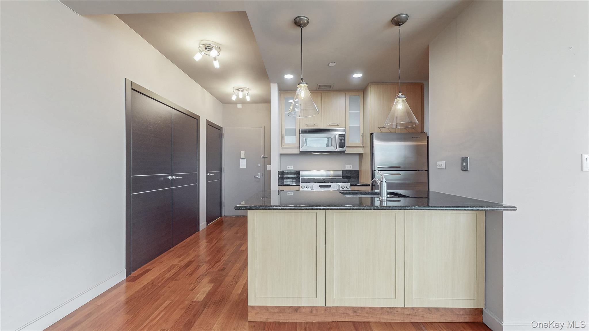 10724 71st Road, Unit 7E Queens, NY 11375 - Photo 8 of 21 Kitchen featuring a peninsula, dark stone counters, glass insert cabinets, light wood-style flooring, and stainless steel appliances