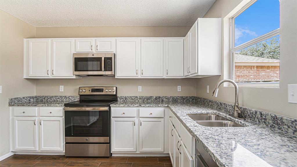8732 Hunters Point Way Fort Worth, TX 76123 - Photo 10 of 24 a kitchen with granite countertop a sink a stove and microwave