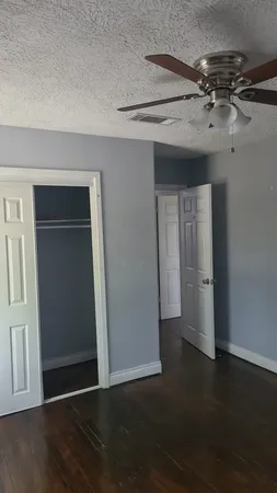 an empty room with wooden floor chandelier fan and windows