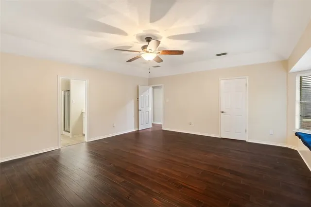 a view of an empty room with wooden floor and a ceiling fan