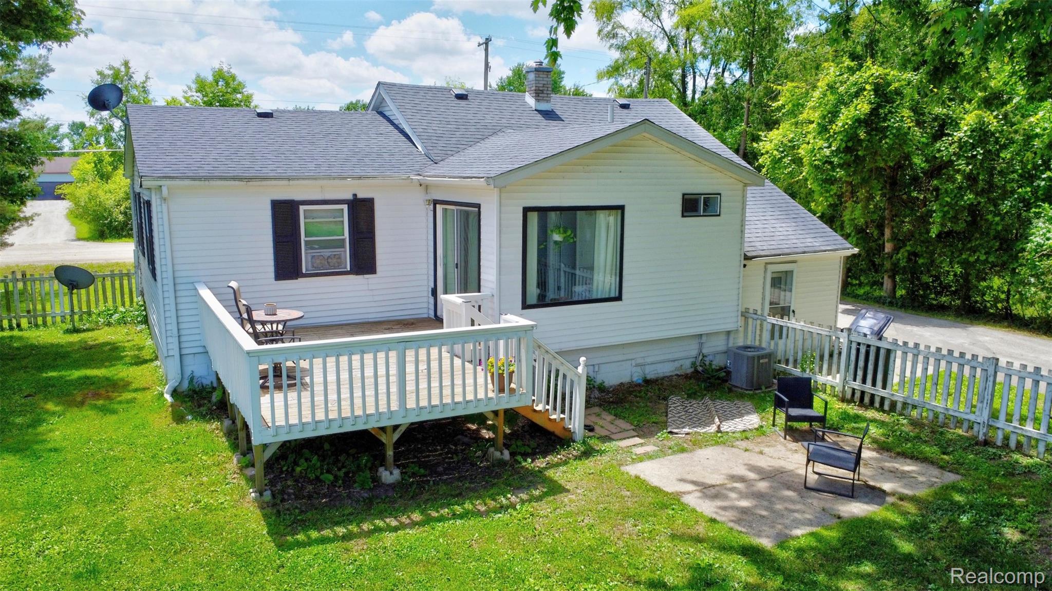 5244 Oleksyn Road Flint, MI 48504 - Photo 46 of 70 Rear exterior featuring a spacious wooden deck with white railings, a ground-level concrete patio, and a white picket fence