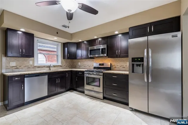 a kitchen with stainless steel appliances granite countertop a refrigerator a sink a stove a microwave and wooden cabinets