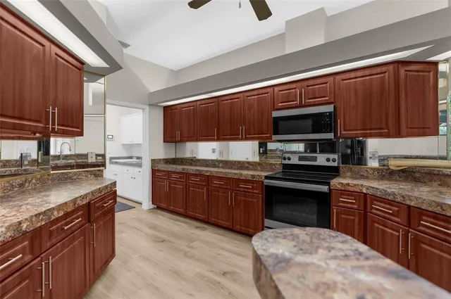 a kitchen with stainless steel appliances granite countertop wooden cabinets a refrigerator a sink a stove and a wooden floors