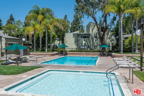 a view of swimming pool with lawn chairs and large trees