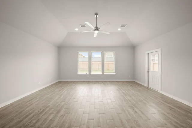 an empty room with wooden floor ceiling fan and windows