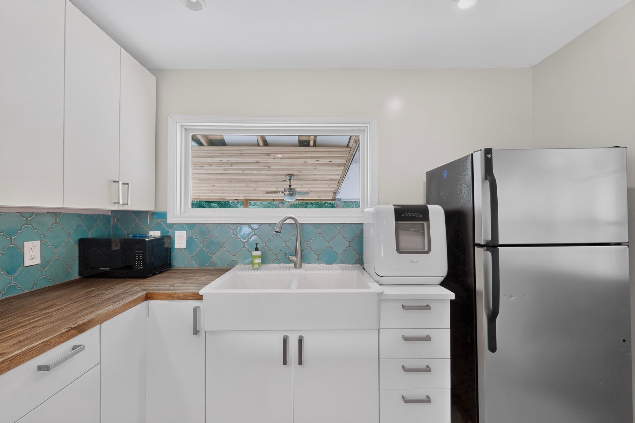 4711 Alf Avenue Austin, TX 78721 - Photo 13 of 34 A well-lit kitchen featuring a classic farmhouse sink, contemporary white cabinetry, and turquoise tile backsplash.