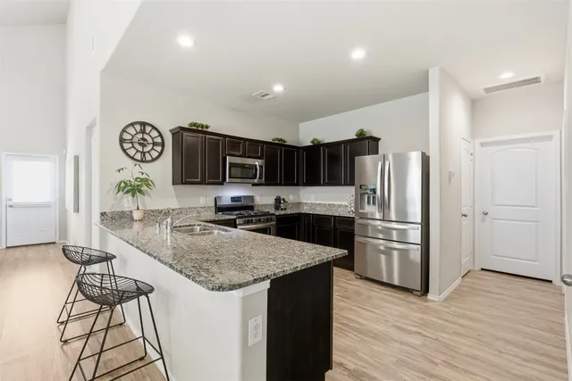 a kitchen with granite countertop a refrigerator a stove a sink cabinets and wooden floor