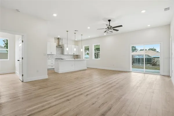 an empty room with wooden floor kitchen view and windows
