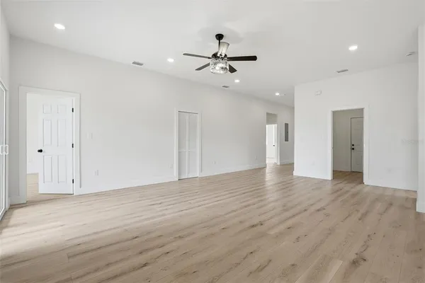 a view of an empty room with wooden floor and a ceiling fan